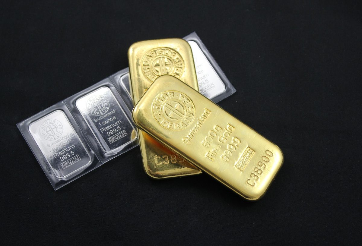 A fine gold bar beside sealed bullion in assay cards